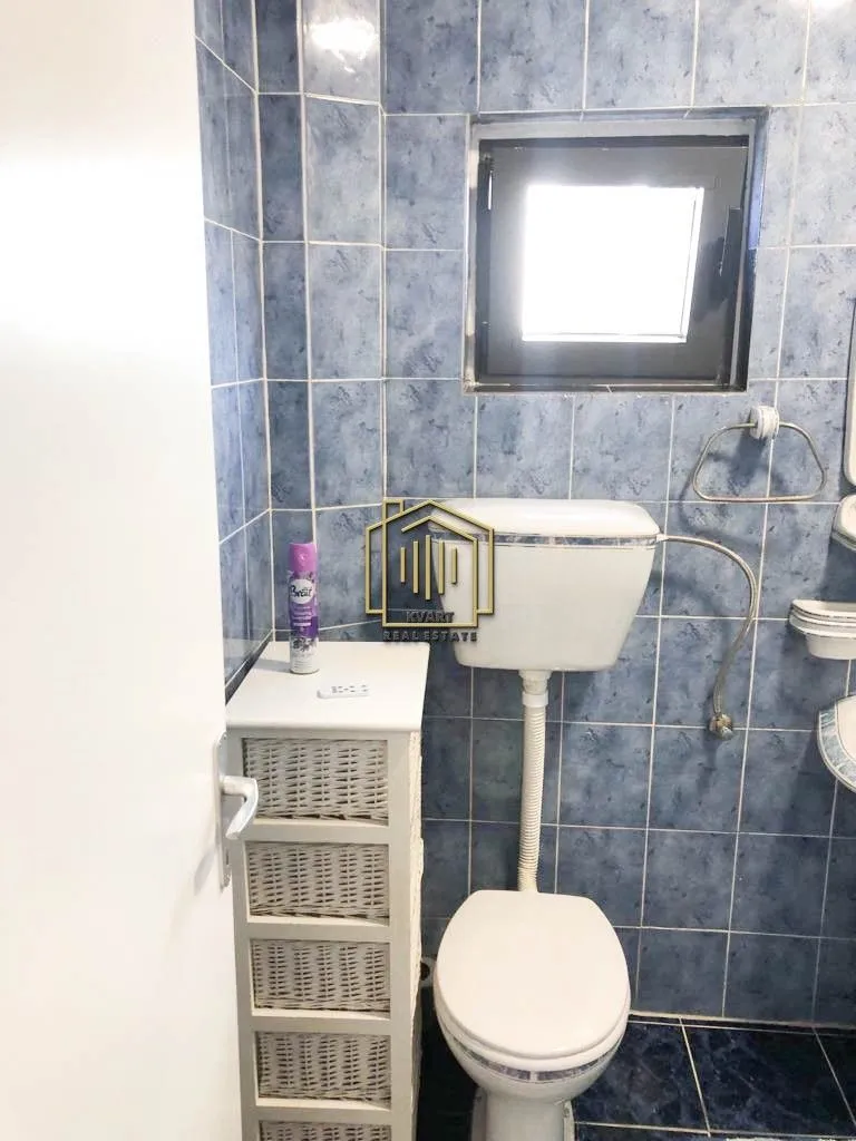 Manje kupatilo obloženo plavim pločicama sa toaletom i malim ormarićem.