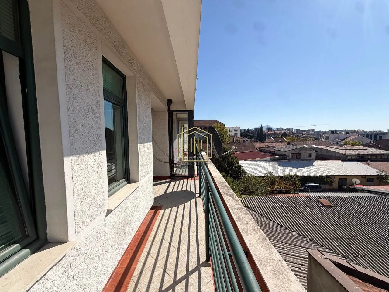 Dugačak balkon sa pogledom na grad i krovove okolnih zgrada.