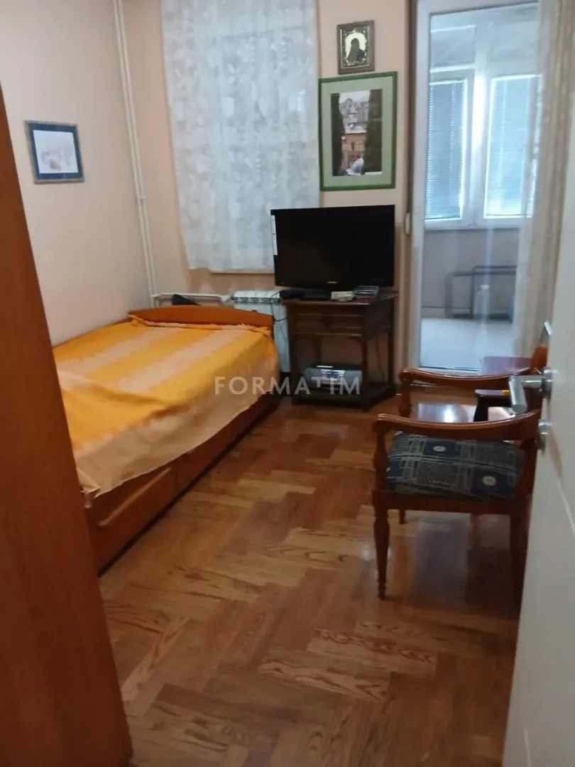 Manja spavaća soba sa krevetom, televizorom i izlazom na terasu.