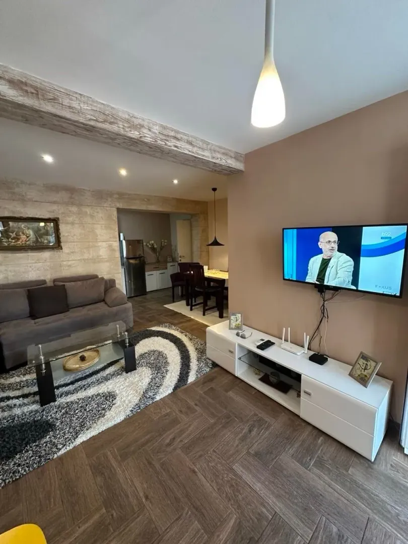 Prostrana dnevna soba sa garniturom i TV-om povezana sa trpezarijom.