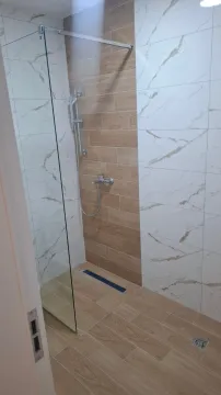 Moderno opremljena tuš kabina sa staklenom pregradom i kombinacijom pločica u dezenu drveta i mermera. - image 3