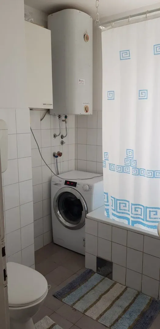 Kupatilo sa veš mašinom, bojlerom i kadom sa zavjesom.