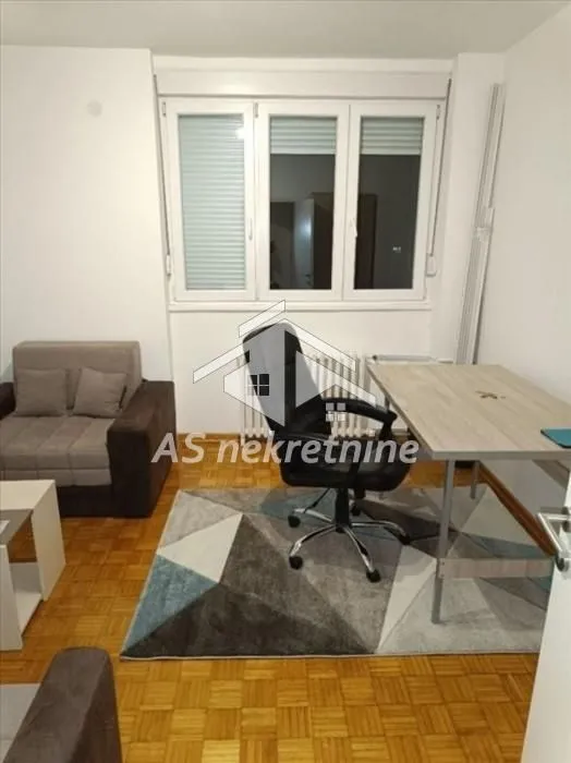 Small room with a desk, armchair, and parquet flooring.