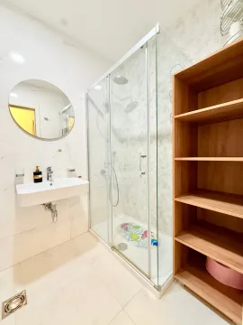 Bright equipped bathroom with a shower cabin, sink, and wooden shelving unit. - image 10