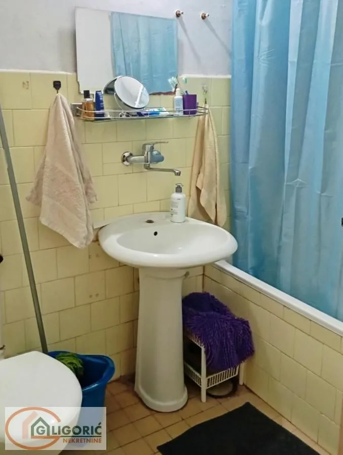 Starije kupatilo sa umivaonikom, kadom i pločicama u svetlim tonovima.
