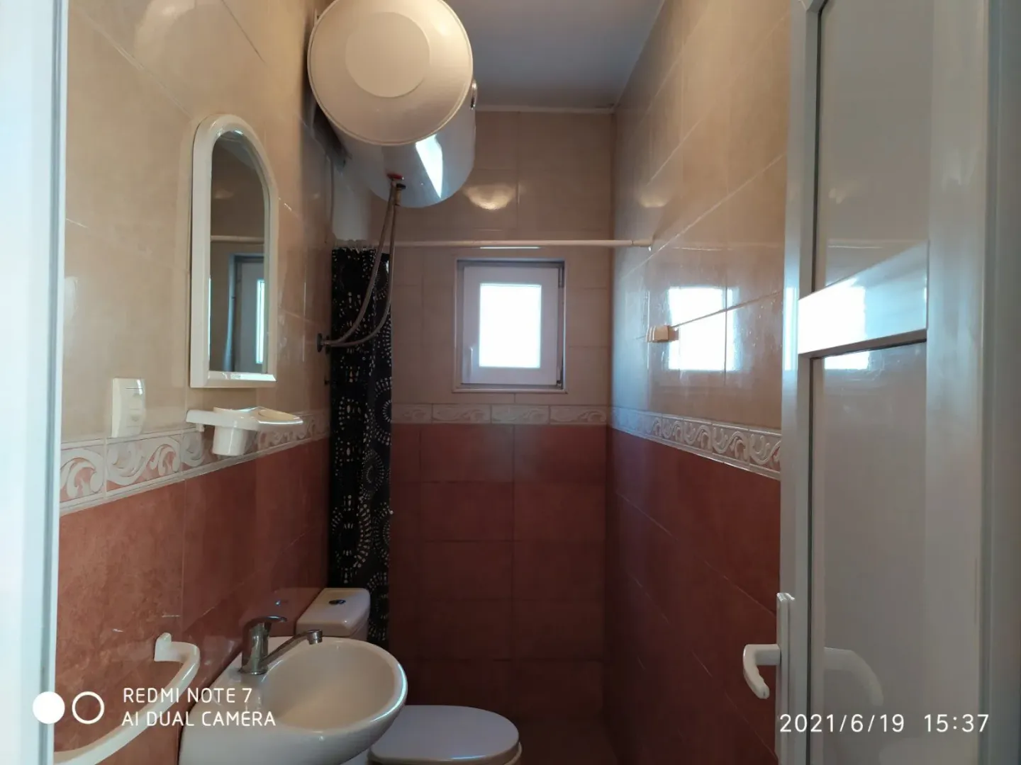 Smaller bathroom tiled with ceramic tiles featuring a sink and a water heater.