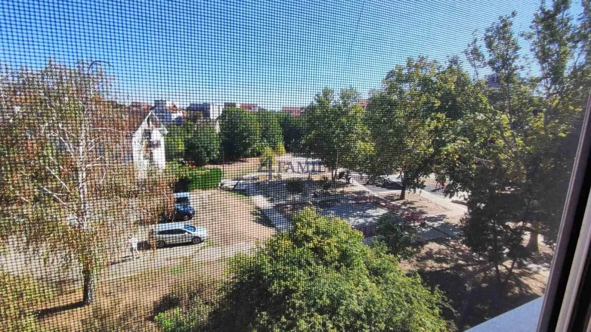 Pogled kroz prozor sa mrežicom na okolno zelenilo i zgrade.