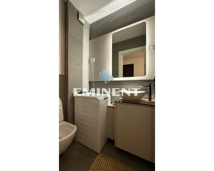 Modernly equipped bathroom with a washbasin, backlit mirror, and washing machine.