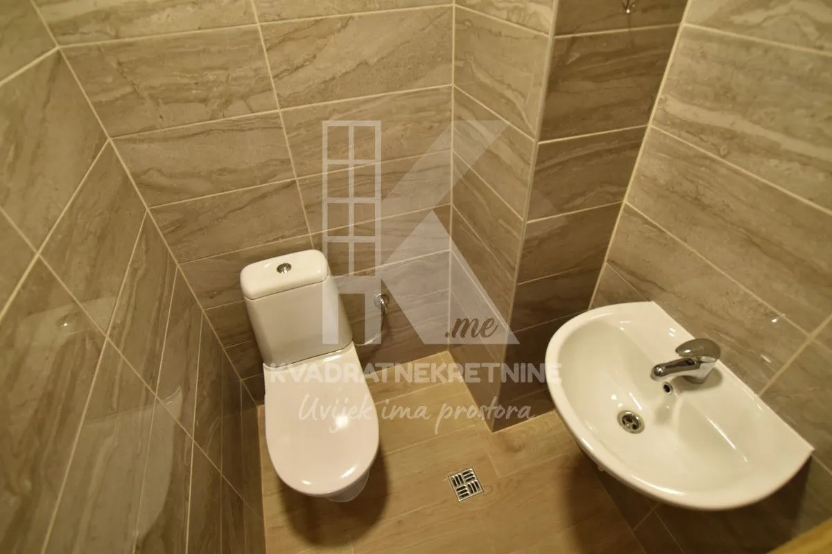 Manje kupatilo obloženo keramičkim pločicama sa WC šoljom i umivaonikom.