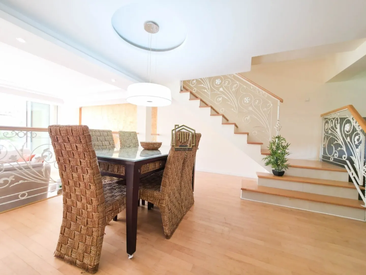 Dining area with a table and wicker chairs, next to the staircase leading to the upper floor.