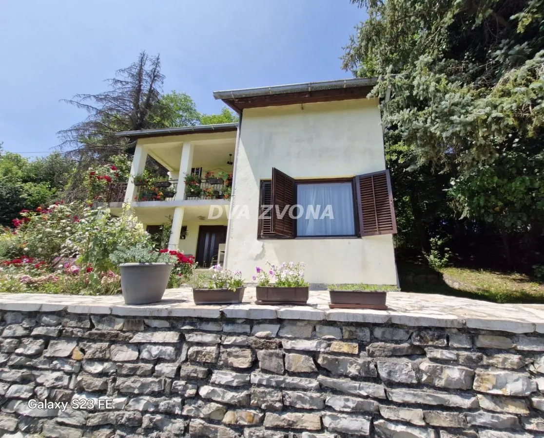Pogled na dvorište i fasadu kuće sa balkonom i zelenilom.