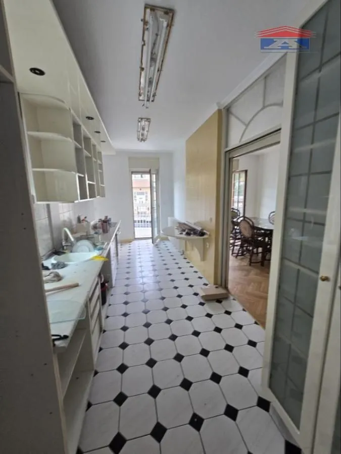 Long kitchen with white cabinetry and black and white floor tiles.