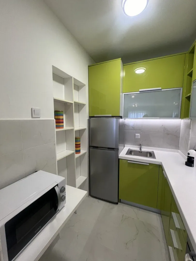 Bright kitchen with green cabinets, a refrigerator, and a built-in sink.