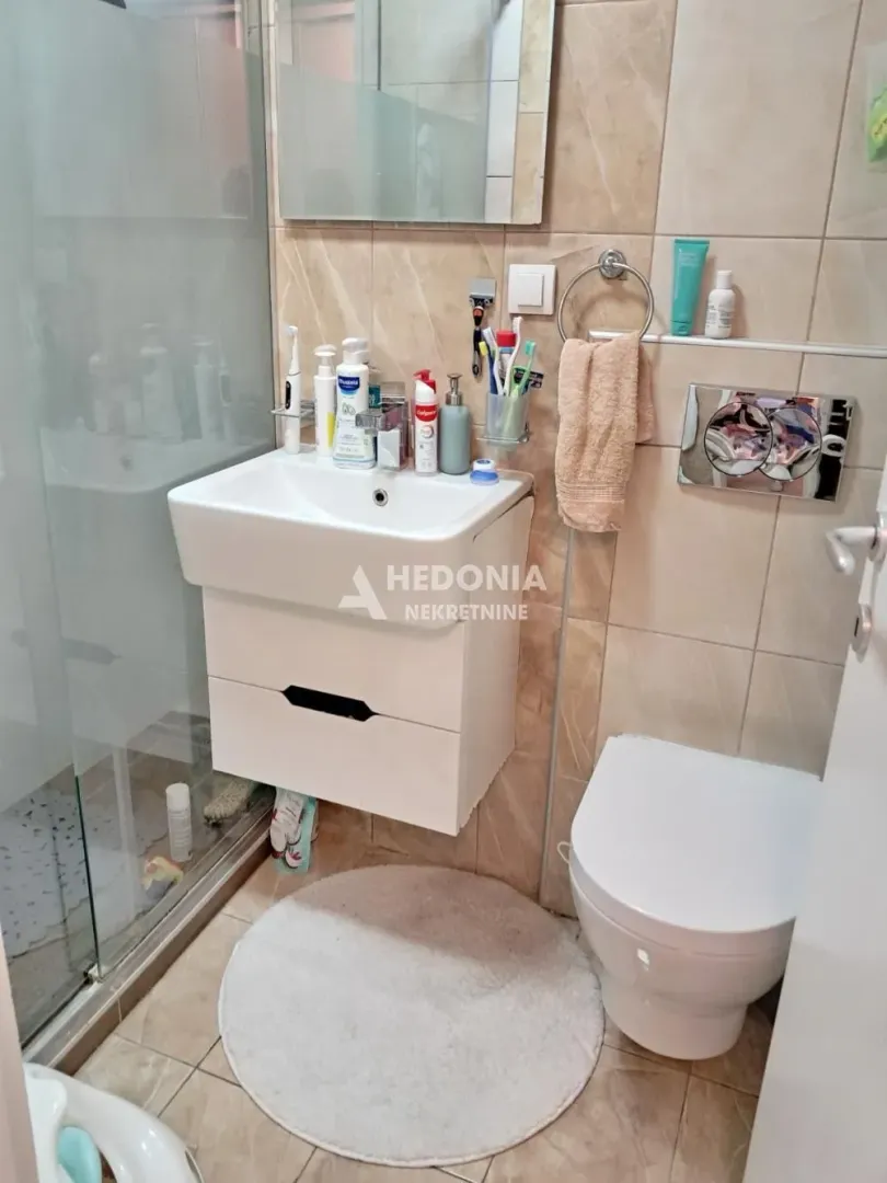 Kupatilo opremljeno umivaonikom, WC šoljom i tuš kabinom.