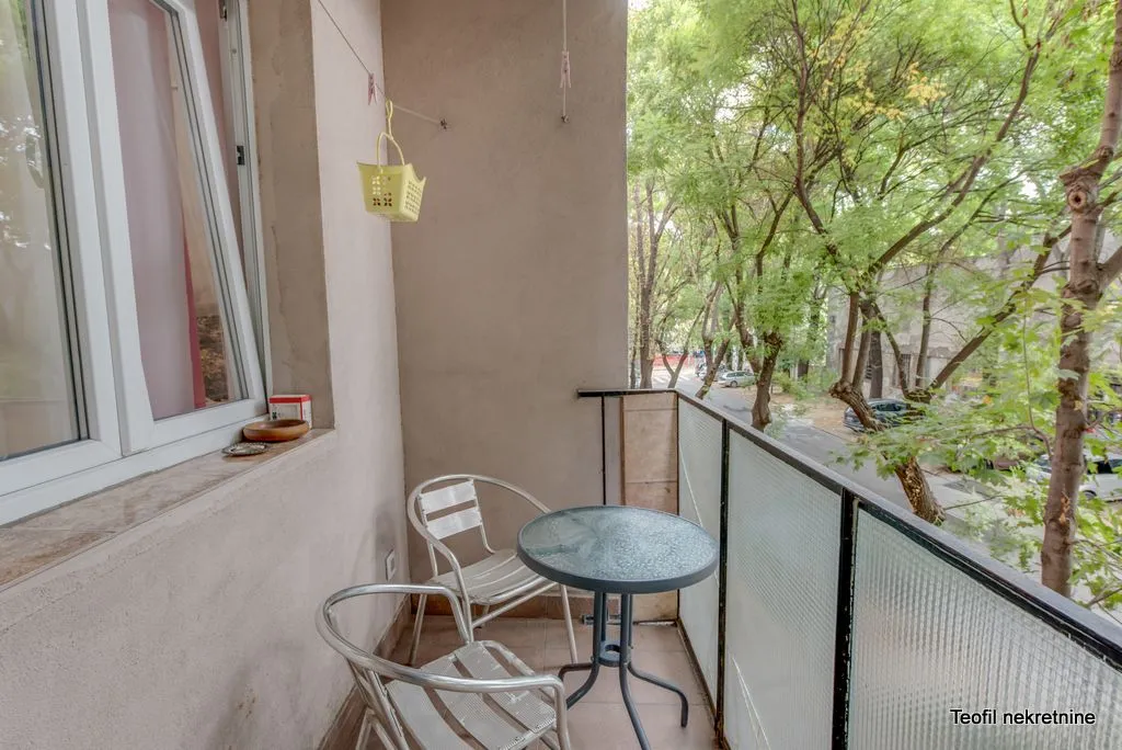 Small furnished balcony with a table and chairs and a view of trees.