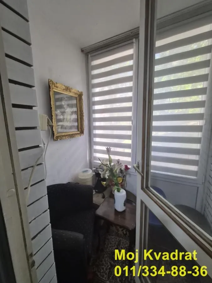 Zastakljeni balkon sa malom foteljom i stočićem.