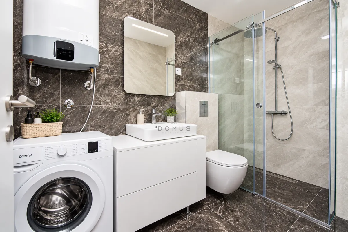 Modern bathroom with a shower cabin, washbasin, and washing machine.
