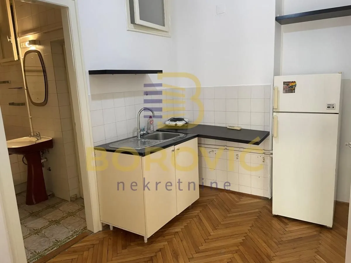 Small kitchen with a sink, countertop and refrigerator, with a view of the bathroom.