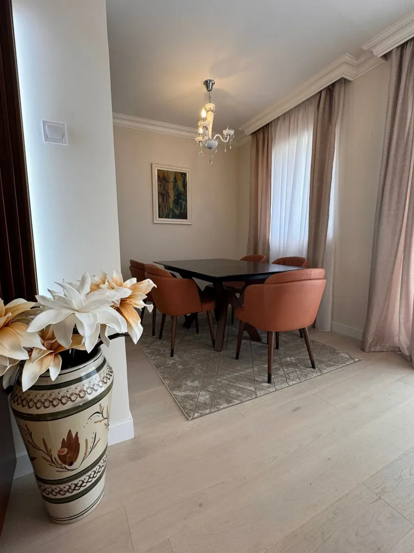 Dining area with a table, chairs, and a decorative vase with flowers in the foreground.