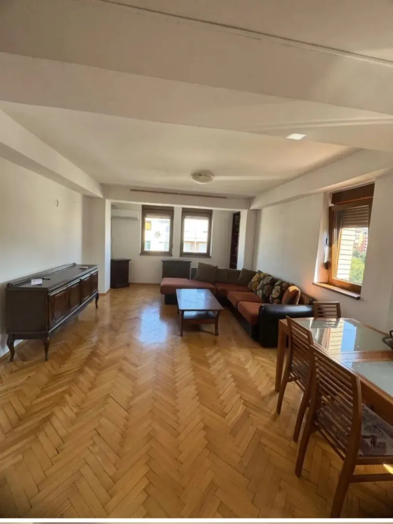 Spacious living room with a sofa set, dining table, and parquet flooring.