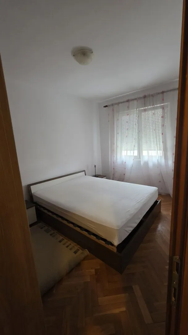 A simply furnished bedroom with a double bed and parquet flooring.