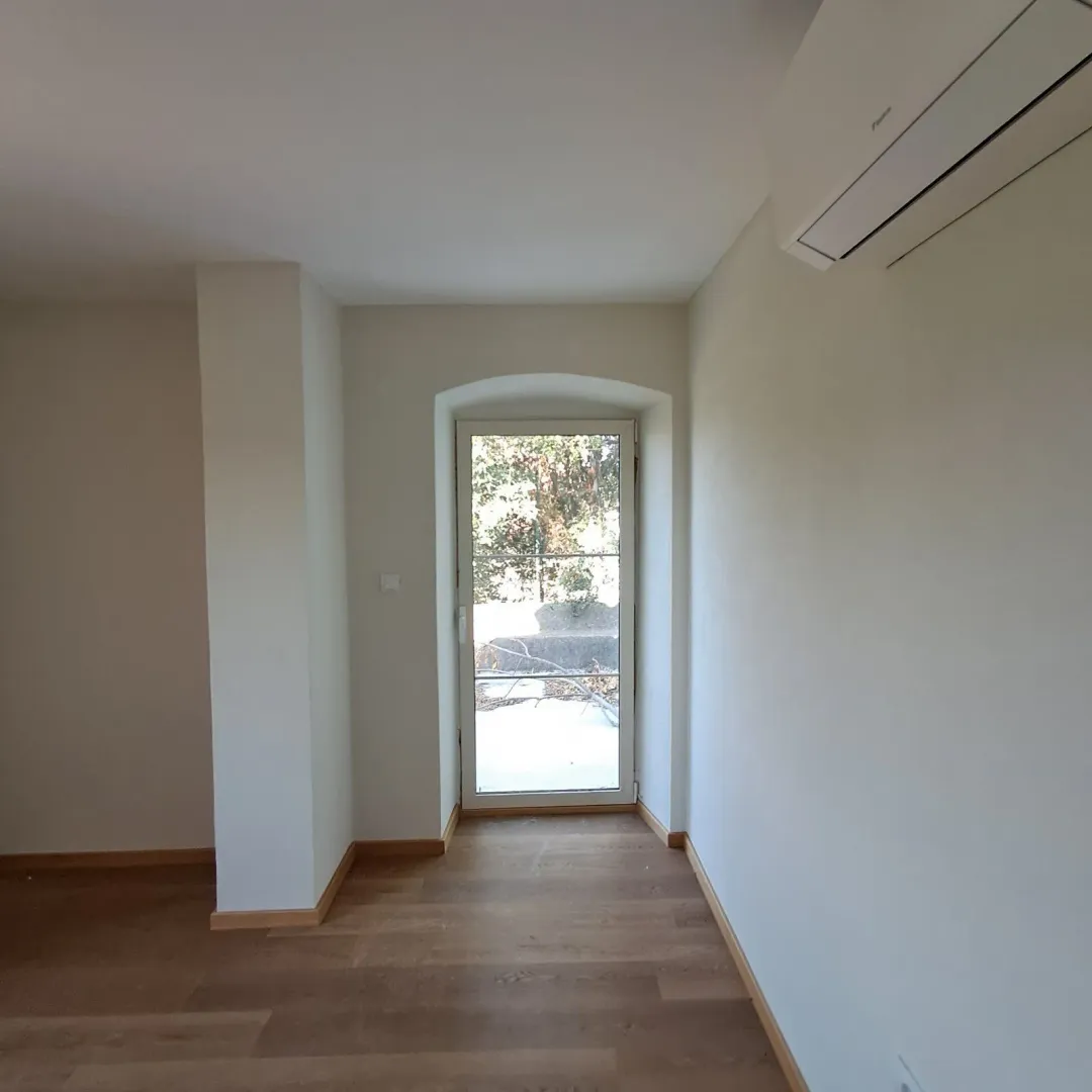 Empty room with wooden flooring, air conditioning unit and a door leading outside.