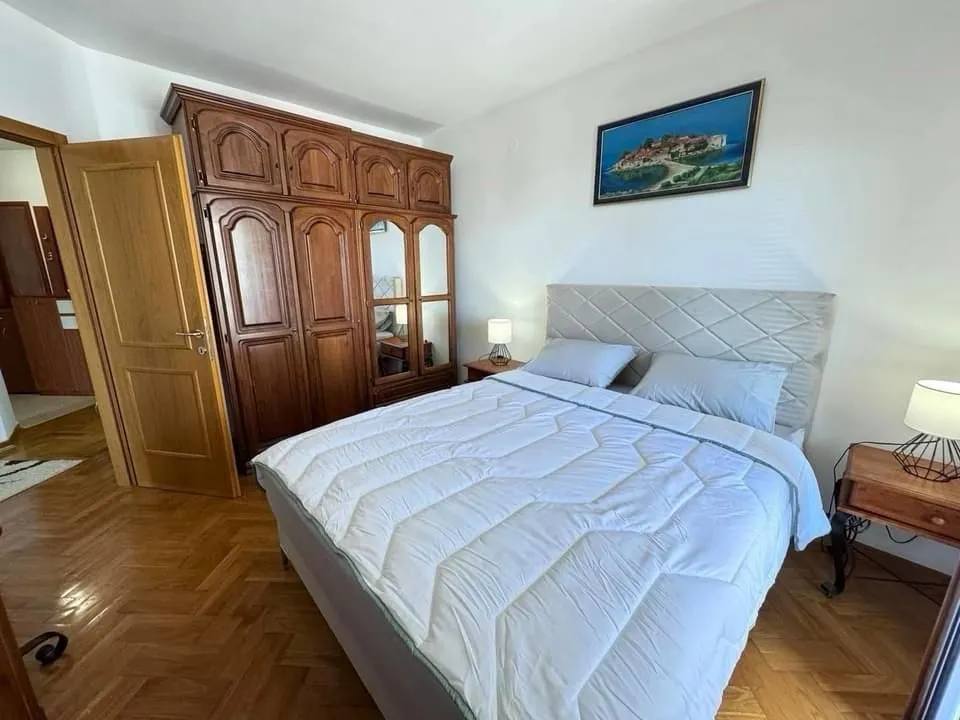 Furnished bedroom with a double bed, large wooden wardrobe, and parquet flooring.