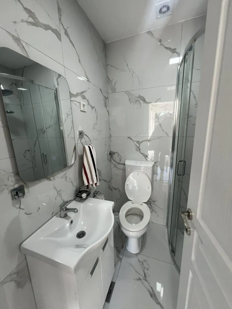 Bright bathroom featuring marble-pattern tiles, a vanity, and a shower.