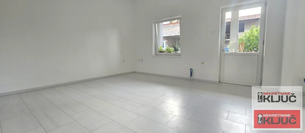 Empty bright room with a tiled floor, window, and door.