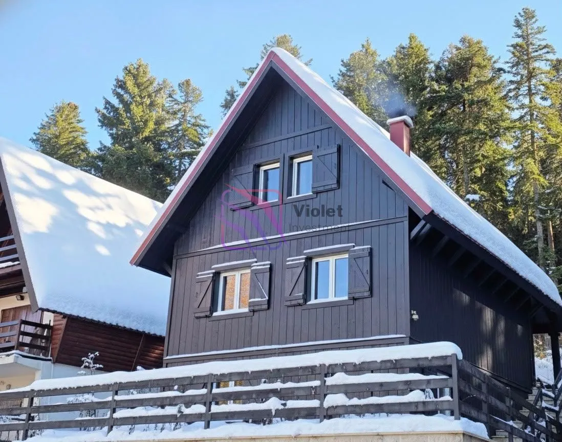 Pogled na drvenu vikendicu u snijegu sa okružujućom šumom.