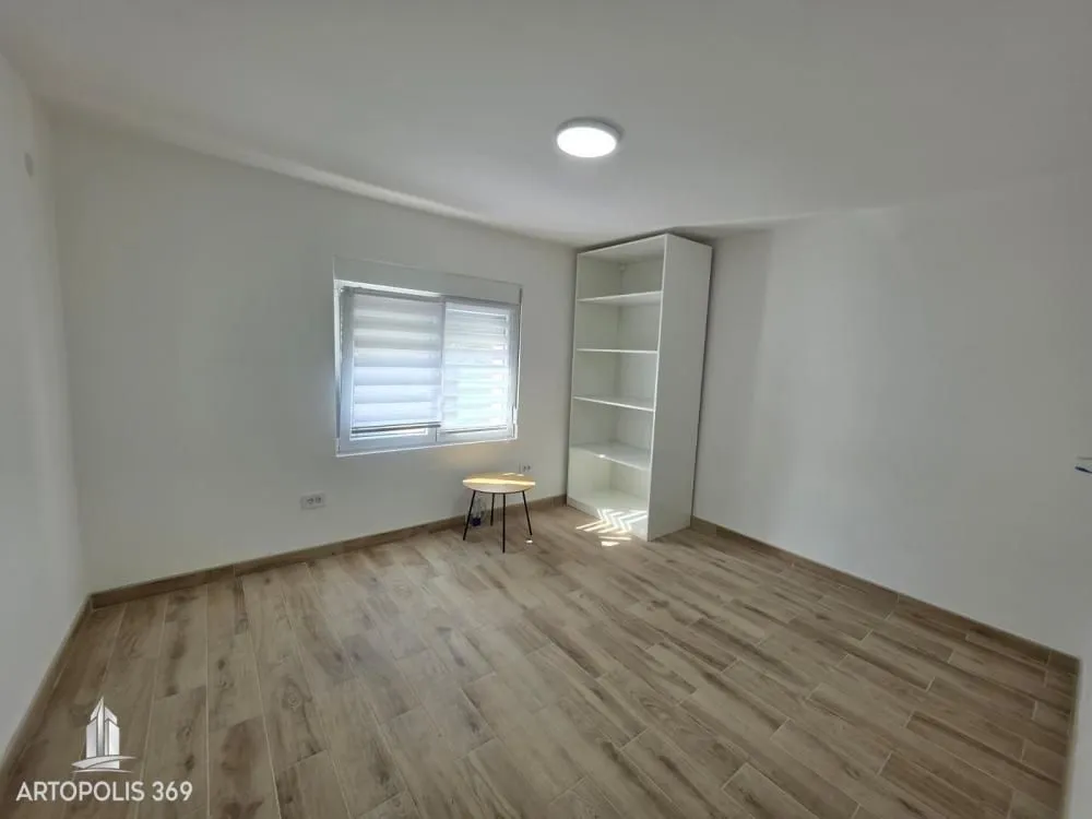 Empty room with white walls, wooden flooring, a window, and a white shelving unit.