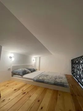 Krevet sa jastucima i pokrivačem u potkrovlju sa drvenim podom. - image 12
