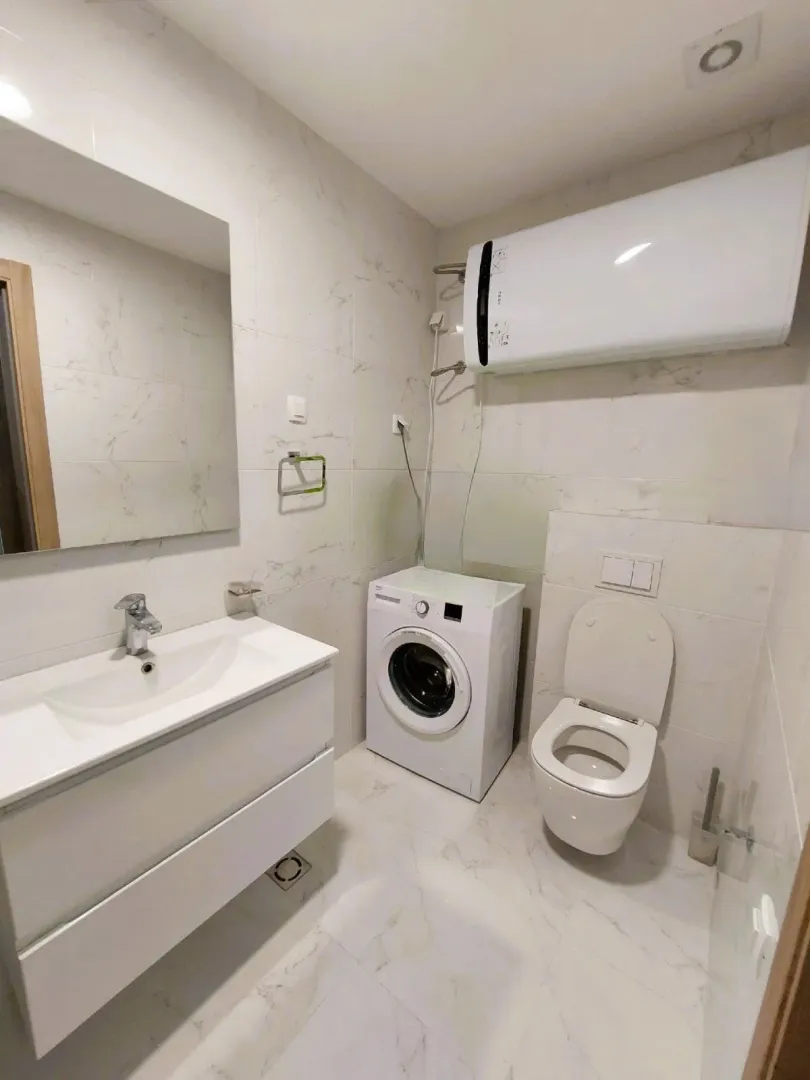 Modern bathroom with a washbasin, washing machine, toilet, and water heater.
