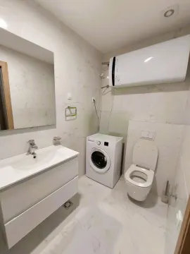 Modern bathroom with a washbasin, washing machine, toilet, and water heater. - image 9