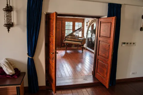 View through wooden doors into a living room with a piano and wooden flooring. - image 6