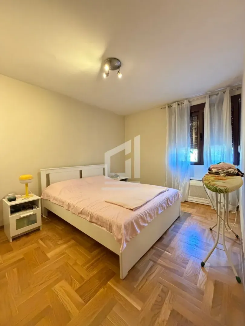 Spavaća soba sa bračnim krevetom, noćnim stočićem i prozorom sa zavjesama.
