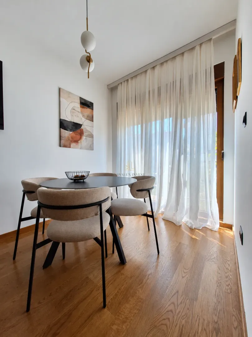 Trpezarija sa okruglim stolom i modernim stolicama pored balkonskih vrata.
