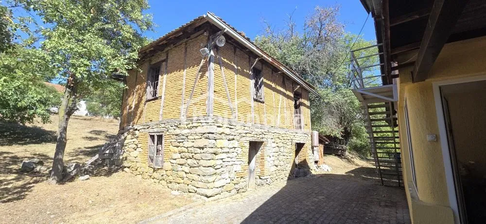 Pogled na spoljašnjost tradicionalne kuće sa kamenim prizemljem i drvenom konstrukcijom na spratu.