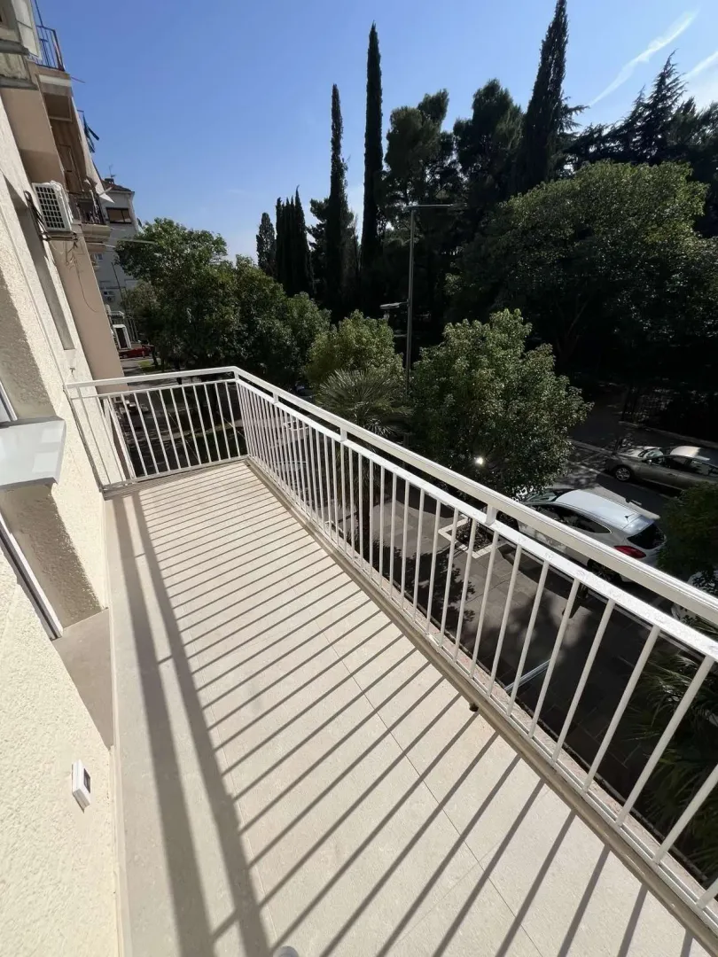 A balcony with a white railing and a view of trees and the street.