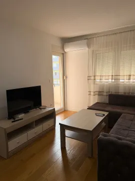 Living room with a sofa, TV stand, and balcony access. - image 2