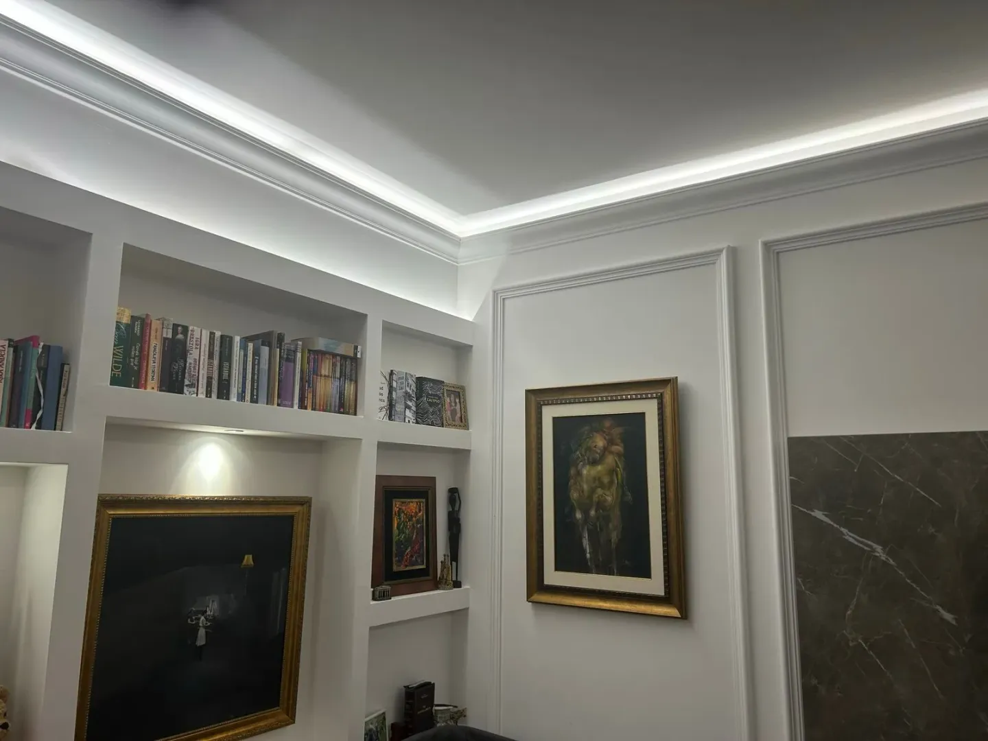 Detalj enterijera sa ugradnim policama, umjetničkim slikama i dekorativnom rasvjetom.