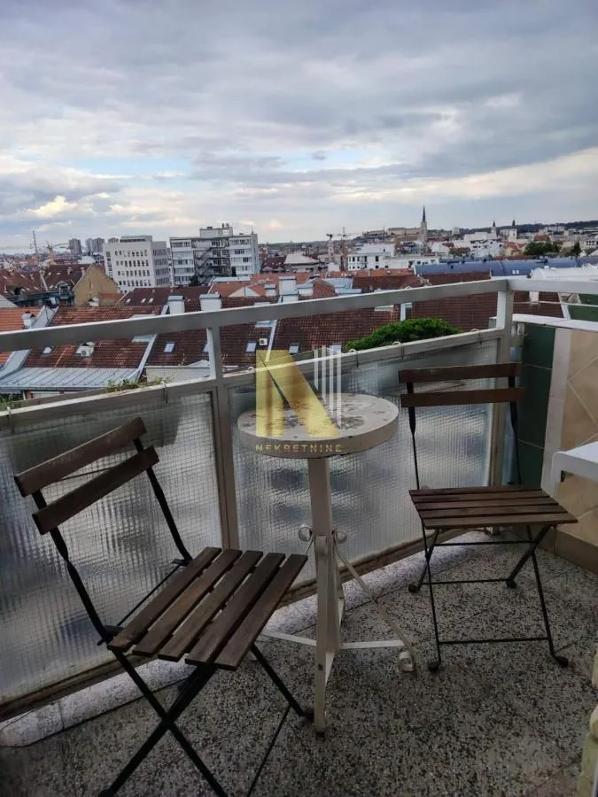 Manji balkon sa stolom i dve stolice i pogledom na grad.