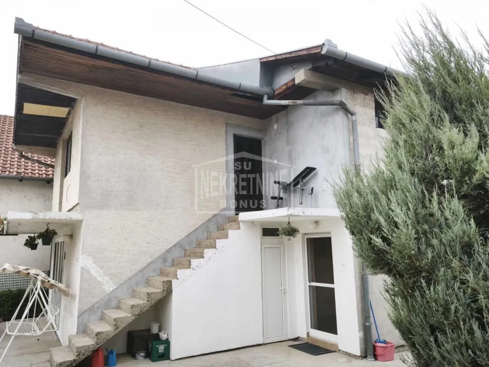 Pogled na spoljašnjost kuće sa spoljnim stepeništem i dvorištem.