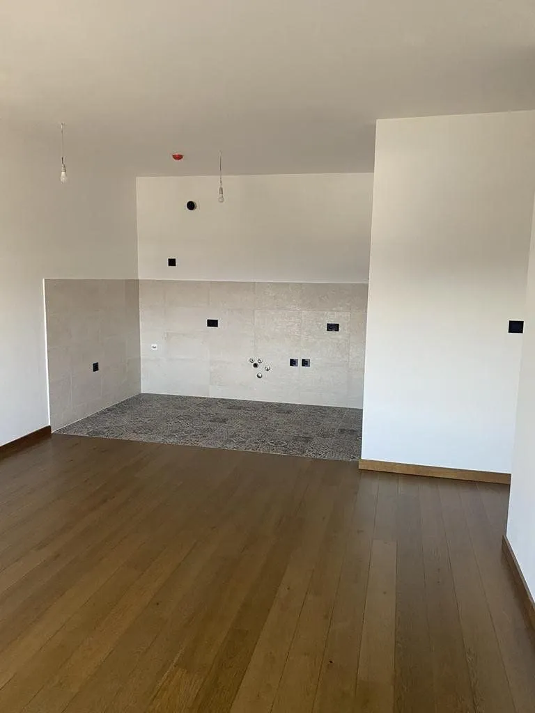 Unfurnished kitchen area with ceramic tiles and wooden flooring in an apartment under construction.