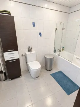 Kupatilo opremljeno toaletom, kadom sa staklenim paravanom i visokim ormarićem. - image 12