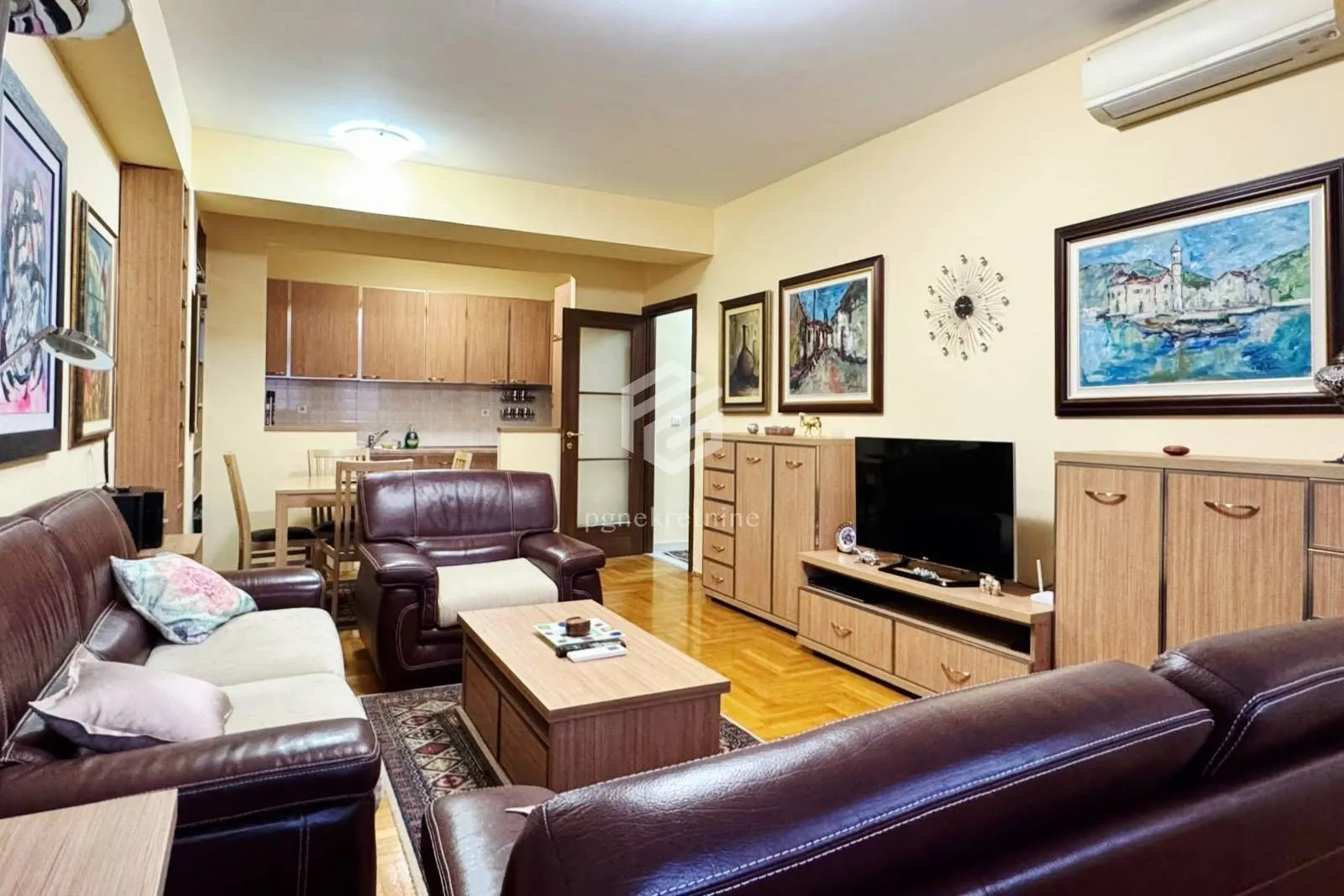 Living room with sofa set, TV, and a view of the dining area and kitchen in the background.