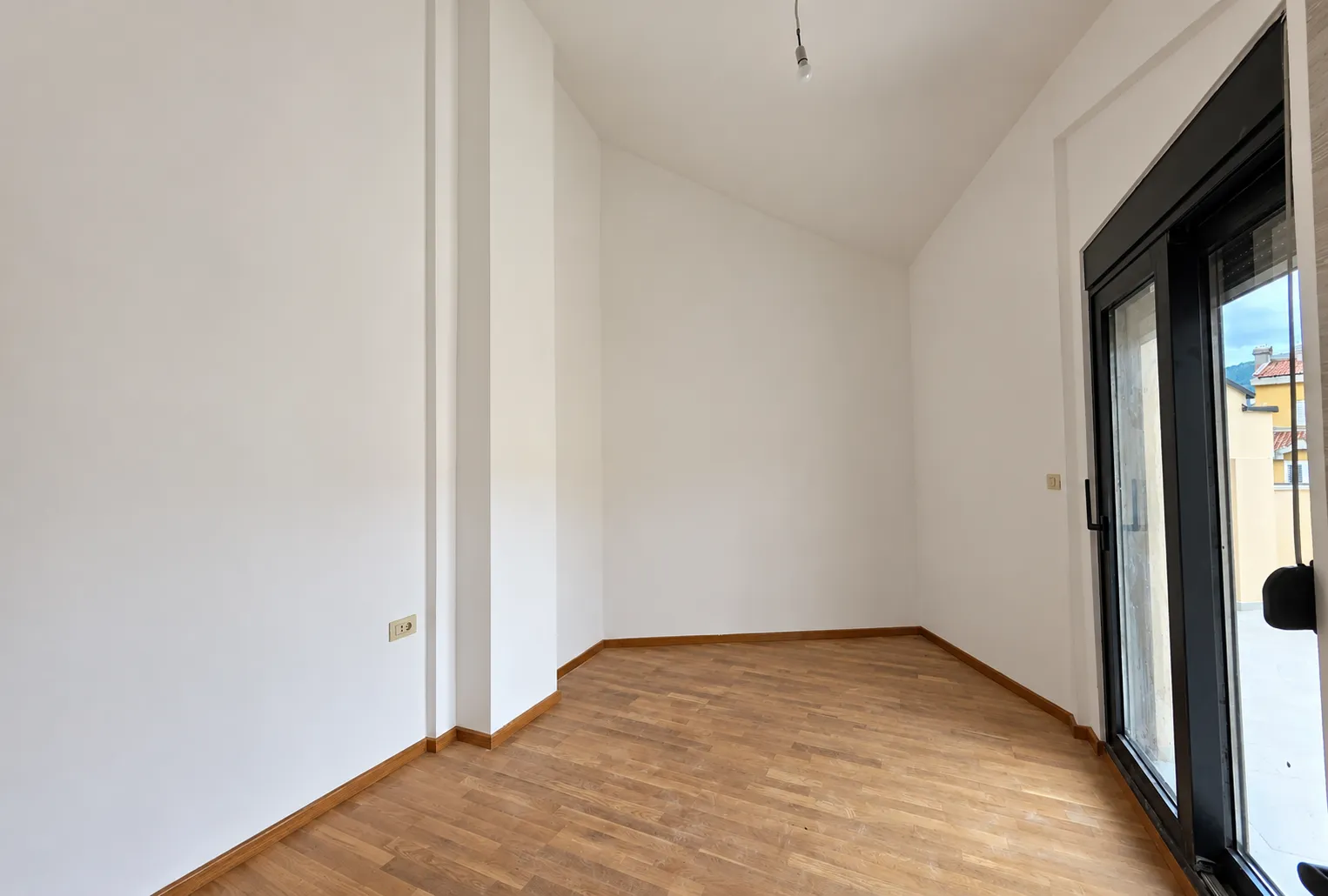 Prazna neopremljena prostorija sa drvenim podom i balkonskim vratima.