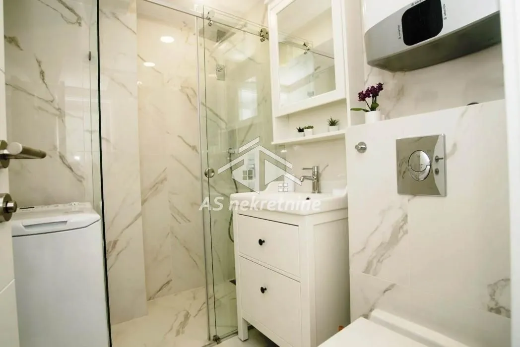 Modern bathroom with a shower cabin, washbasin, and washing machine.