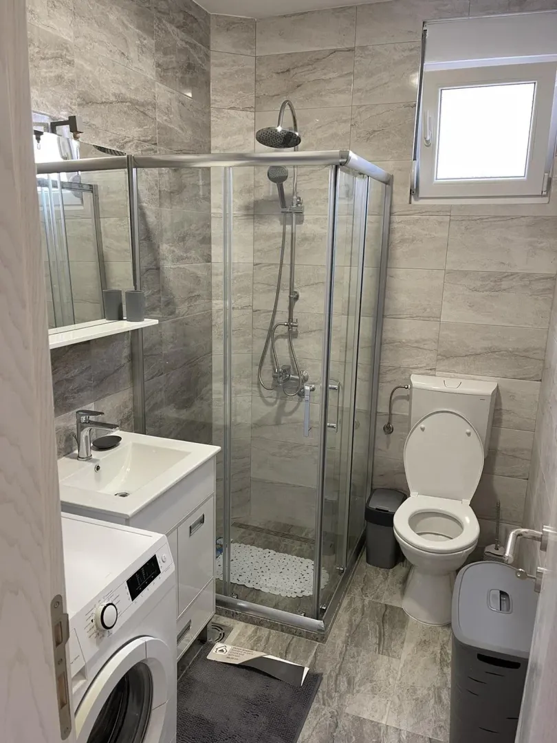 Moderno kupatilo sa tuš kabinom, lavaboom i veš mašinom.