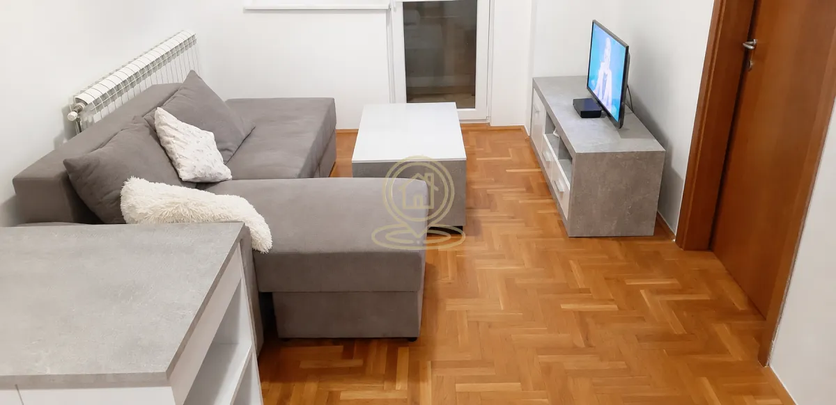 Dnevni boravak sa ugaonom garniturom, TV komodom i parketom na podu.